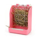 Load image into Gallery viewer, A pink plastic rabbit hay feeder dispenser with a metal grid front and a built in tray for containing messy hay, shown isolated on a white background. This hanging or wall-mounted feeder is designed for bunnies.