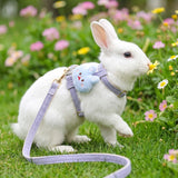 Load image into Gallery viewer, A cute white rabbit smelling a flower outdoors in the grass while wearing a secure purple adjustable bunny harness.