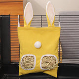 Load image into Gallery viewer, A small yellow hanging rabbit grass pellet feeder with bunny ears and a fluffy tail, featuring two dispensing windows filled with grass pellets, attached to a black wire cage.